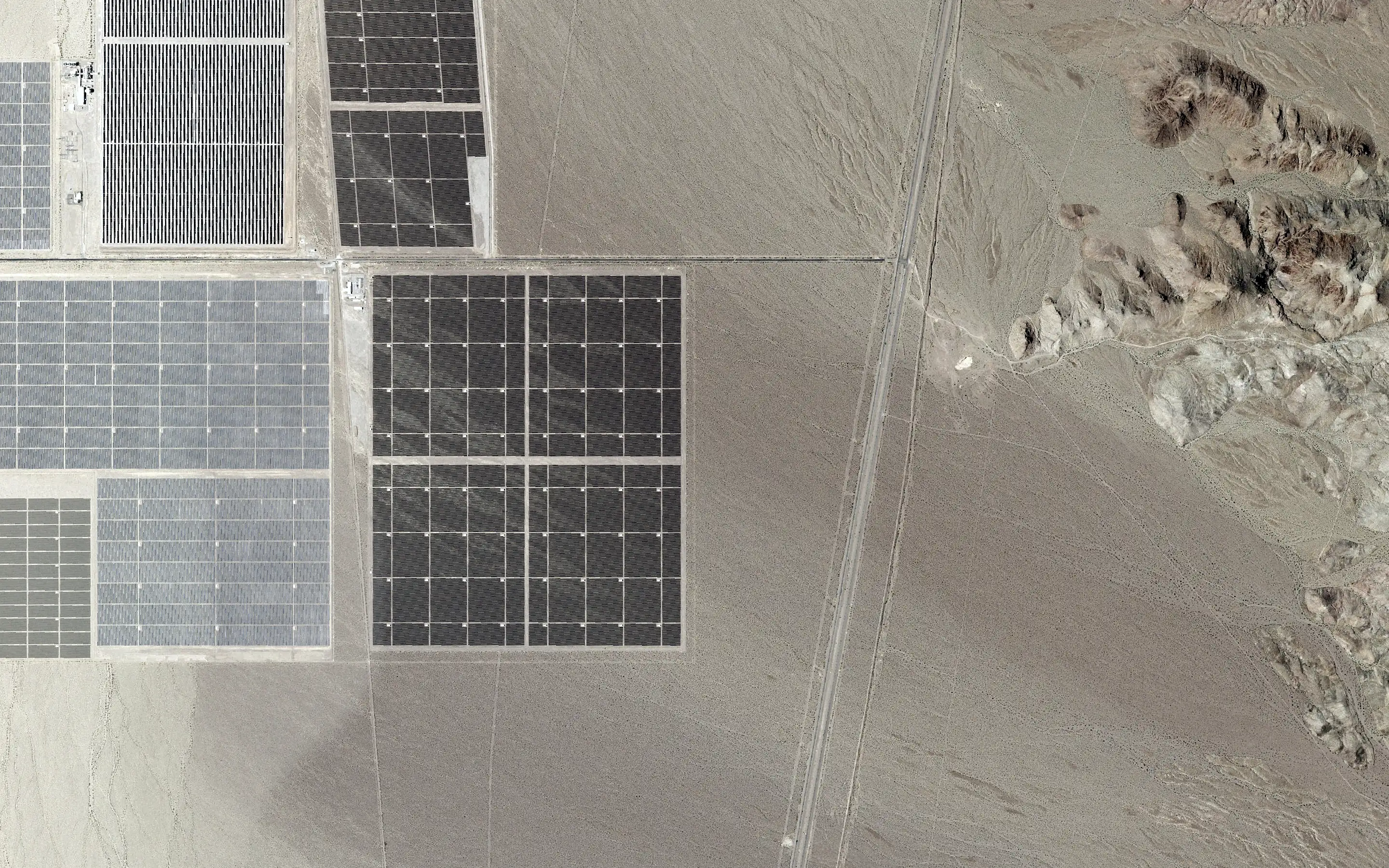 Aerial view straight down: a transmission corridor crossing a desert valley.