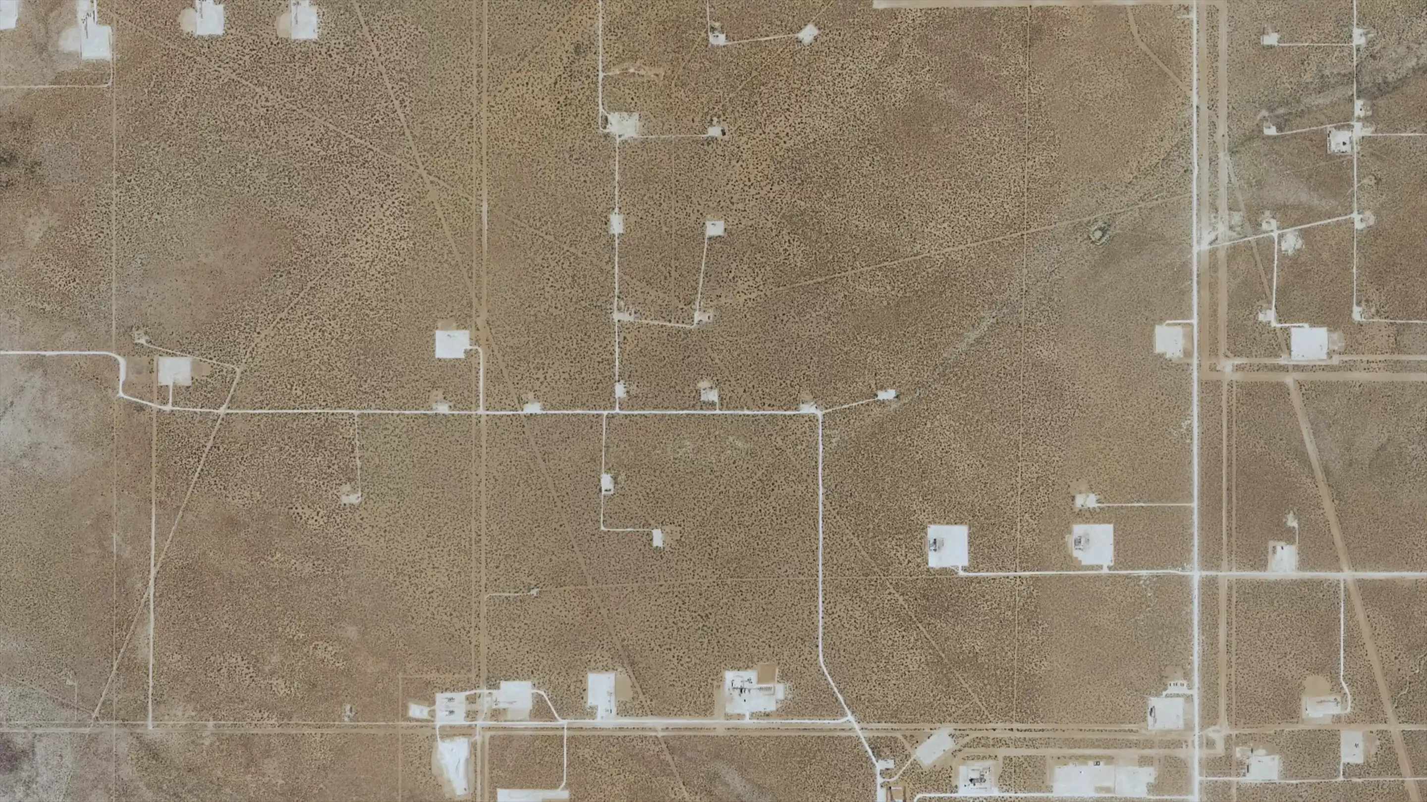 Aerial view straight down: roads and pads across open range around one section.