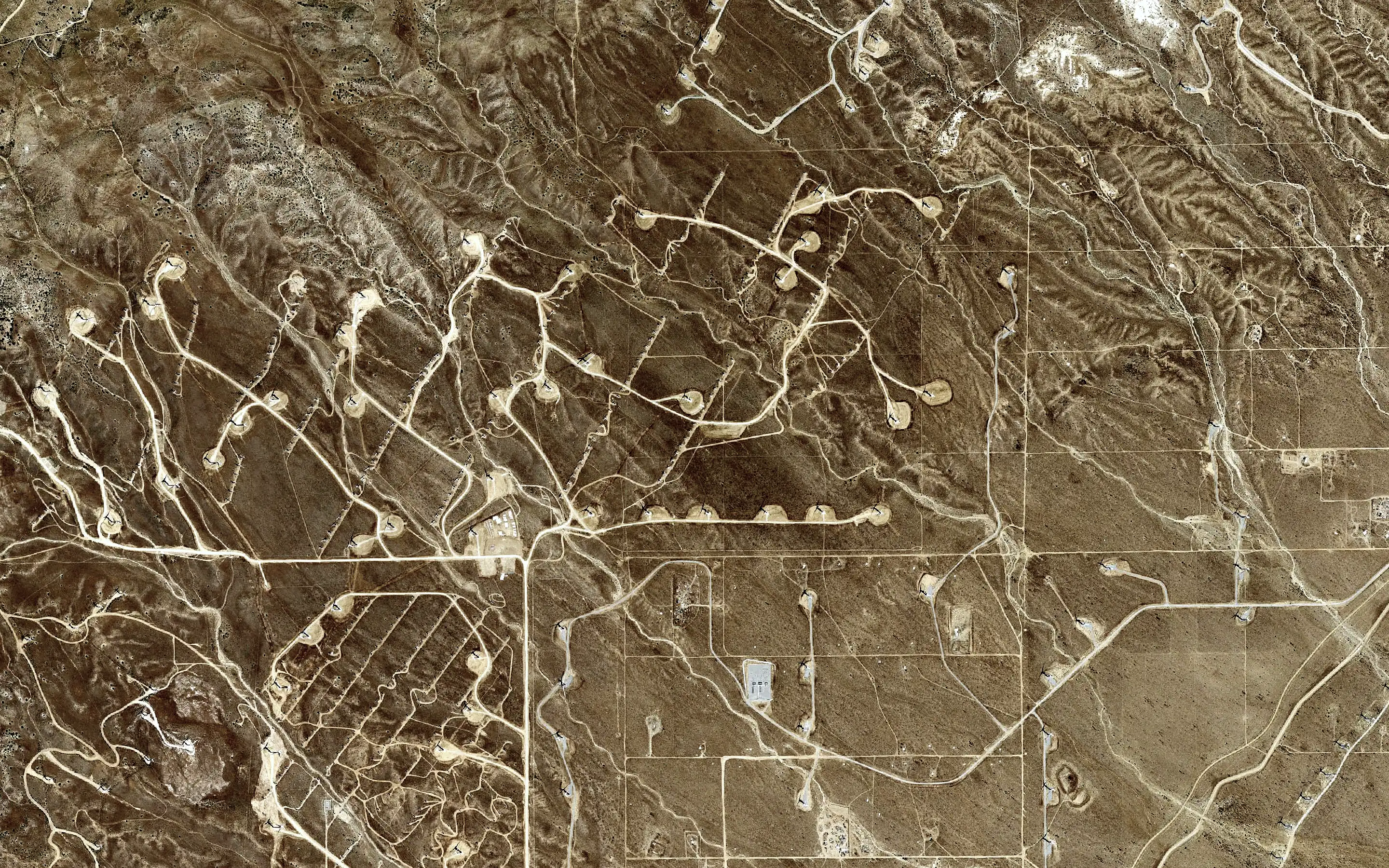 Aerial view straight down: wind turbine pads and access roads across hills.